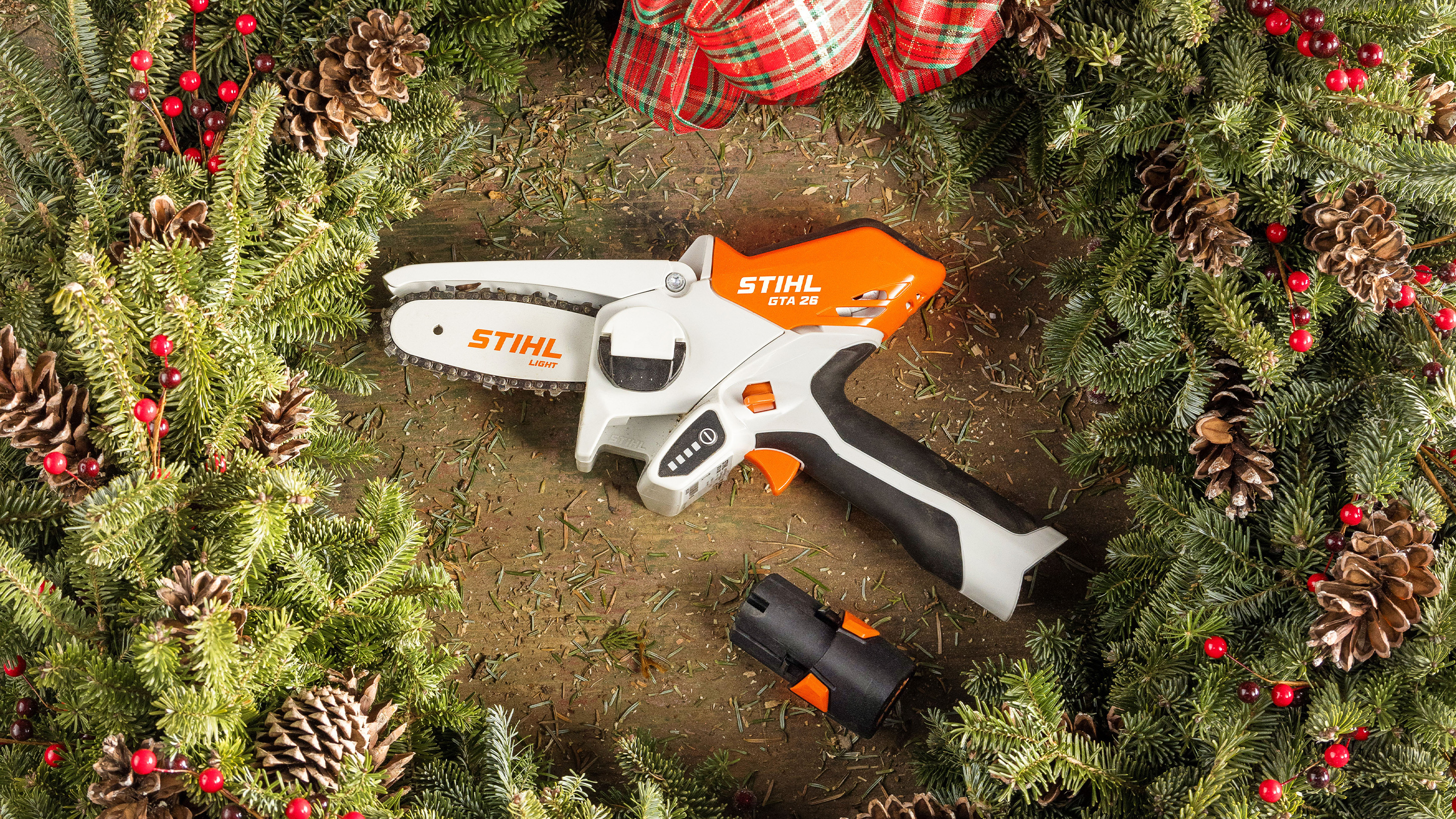 STIHL GTA 26 in einem Adventskranz, umgeben von Tannengrün, Tannenzapfen und einem Schleifenband mit Weihnachtskarte