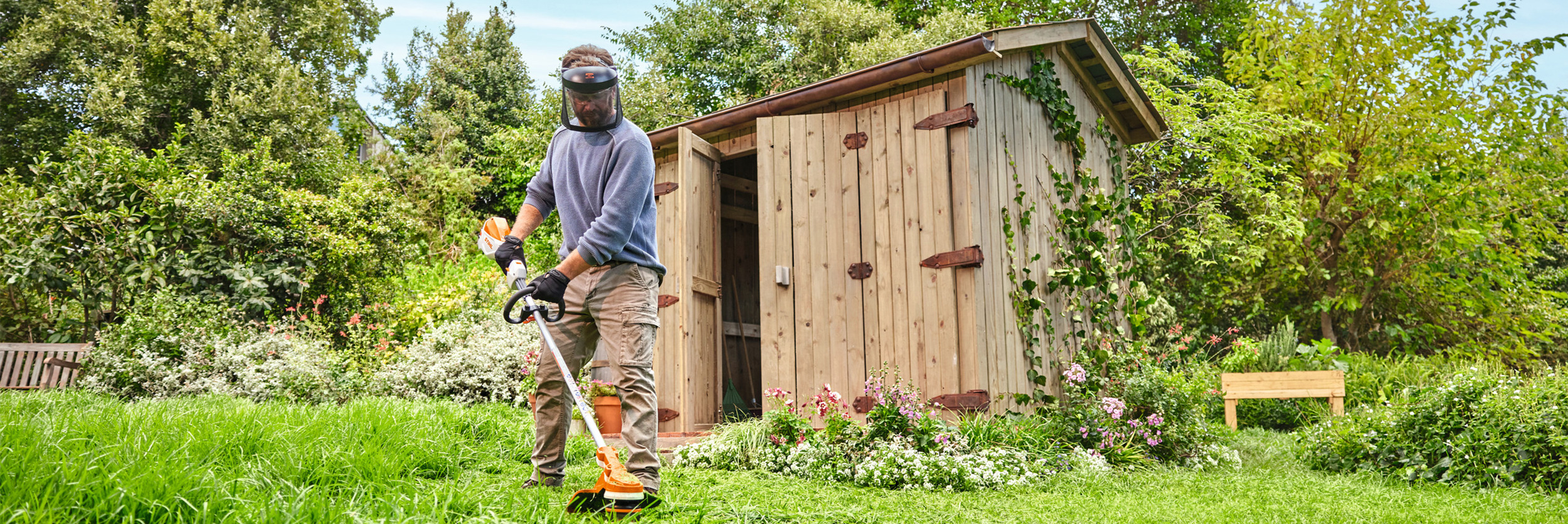 Ein Mann trimmt mit dem STIHL Akku-Freischneider FSA 70 R das Gras in seinem blühenden Garten