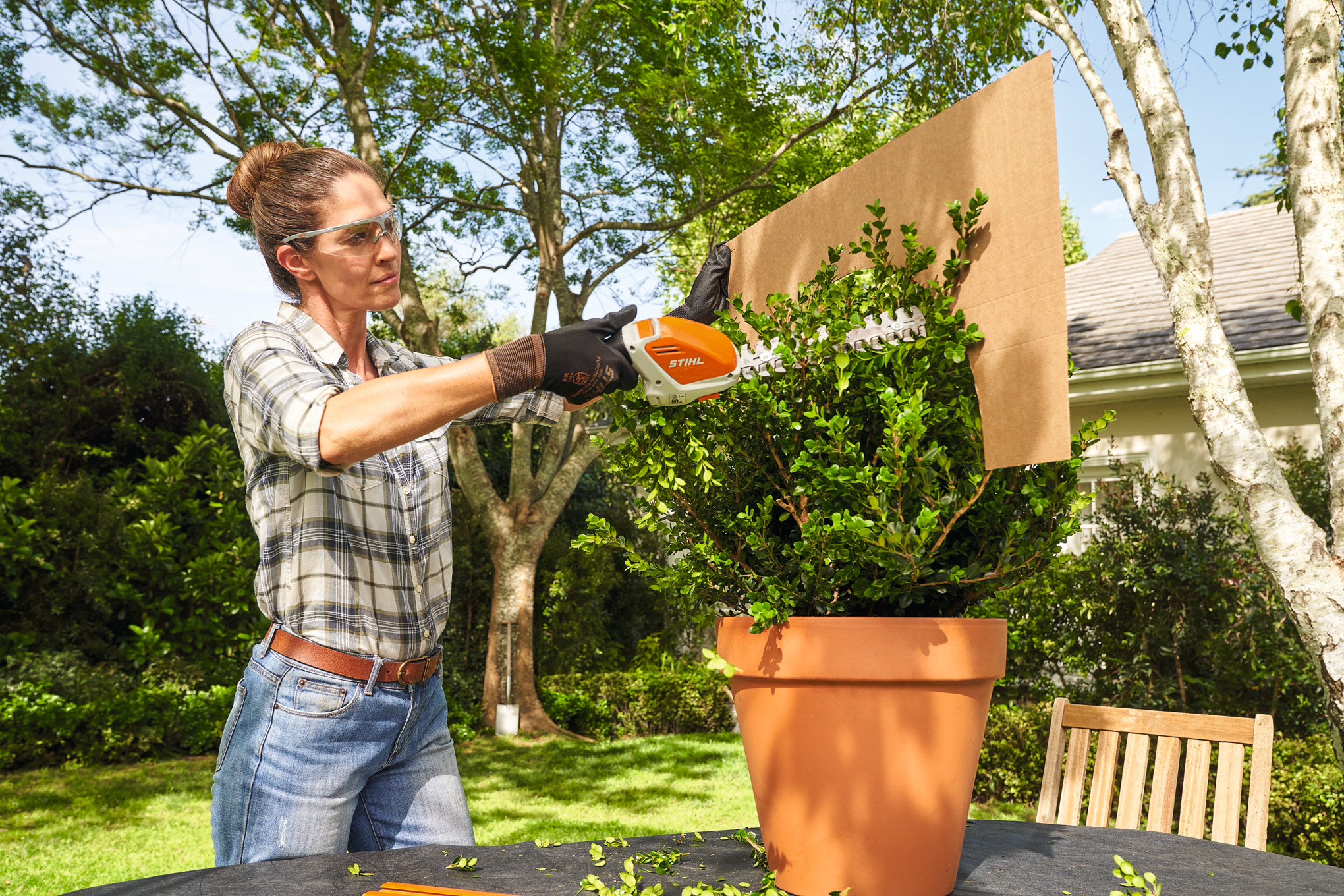 Eine Frau schneidet den Buchsbaum mit der Akku-Strauchschere STIHL HSA 26 mithilfe einer Pappschablone in Kugelform 