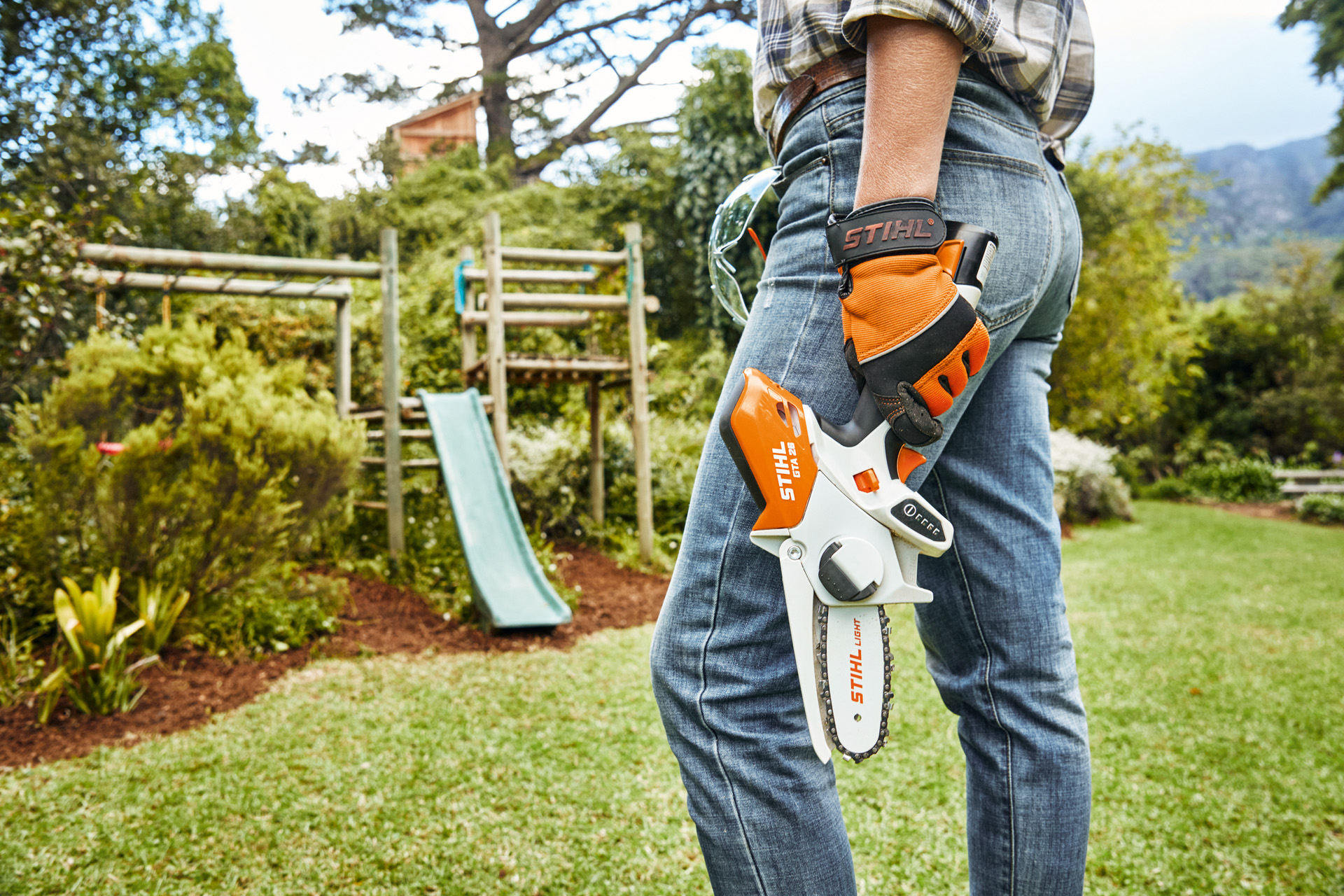 Person mit STIHL Akku-Gehölzschneider GTA26 steht im Garten vor einer Rutsche